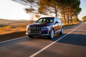 Audi SUV driving on a country road lined with trees and open fields, captured at speed on a sunny day.