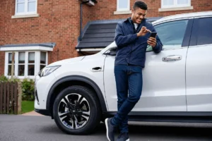 Person leaning on their white car, using their phone