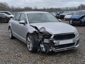 Damaged silver saloon car in a fenced salvage compound after being declared a total loss