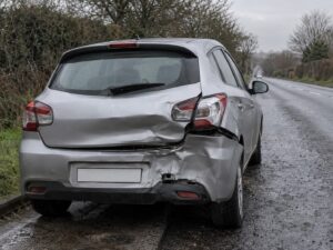 Silver hatchback with rear end damage stopped at the side of a wet British road, blank number plate